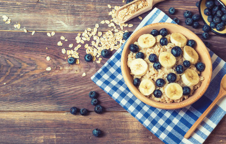 Oatmeal with blueberries and banana in wooden bowl on rustic wooden background. Healthy breakfast. Top view.の写真素材