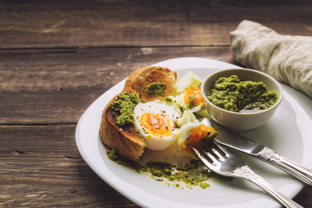 Boiled egg with toasted bread and pesto sauce on rustic wooden background. Selective focus.