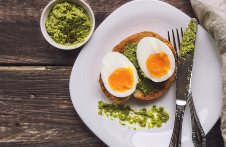 Toast with soft-boiled egg and pesto sauce on rustic background. Top view.