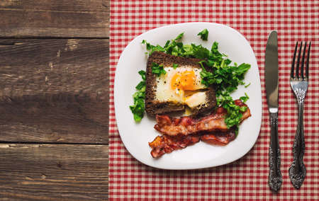 Fried egg in rye bread with bacon and parsley on rustic wooden background. Top view.の写真素材