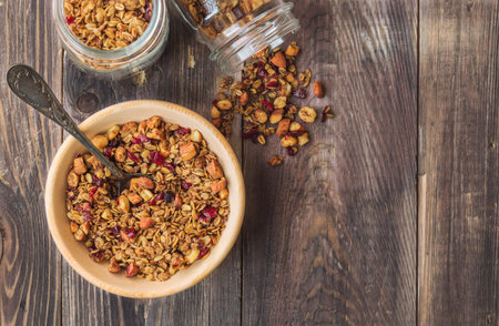 Homemade granola, muesli with nuts and dried cranberries in wooden bowl on rustic wooden background. Healthy breakfast. Top view.の写真素材