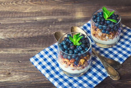 Homemade granola; muesli with blueberry and yogurt in glasses on rustic wooden background. Healthy breakfast.の写真素材