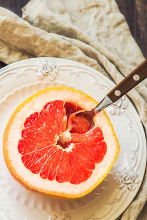 Half a grapefruit on vintage plate with spoon on rustic wooden background. Healthy breakfast.の写真素材