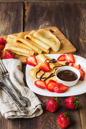 Fresh homemade crepes with strawberries and chocolate sauce on rustic wooden background.の写真素材