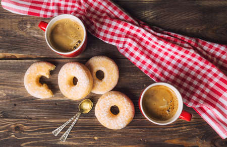 Two red mugs with coffee and donuts on rustic wooden background. Top view.の写真素材