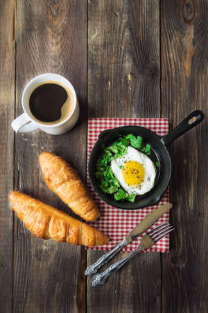 Traditional breakfast with coffee, croissants and fried egg in iron skillet on rustic wooden background.の写真素材