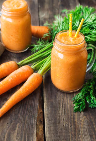 Fresh carrot smoothie in glass jars on rustic wooden background.の写真素材