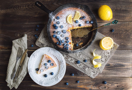 Fresh homemade lemon pie with blueberries in iron skillet on rustic wooden background. Top view.