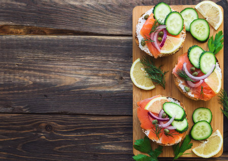 Sandwiches with smoked salmon, red onion, capers, cucumber and lemon on rustic wooden background. Top view. Copy space area.の写真素材