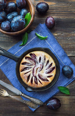 Fresh homemade plum cake in iron skillet on rustic wooden background. Top view.の写真素材