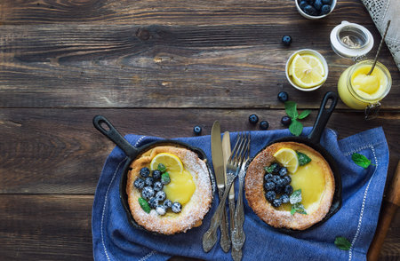 Fresh homemade Dutch Baby pancake with lemon curd and blueberries in iron skillets on rustic wooden...