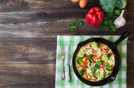 Frittata with broccoli and red pepper in iron skillet on rustic wooden background with ingredients. Top view. Copy space area.の写真素材