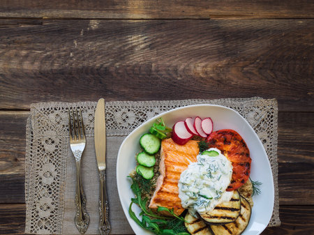 Grilled salmon, eggplants and tomatoes with quinoa and tzatziki sauce on rustic wooden