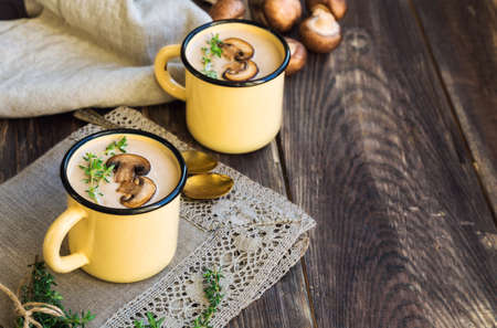 Creamy mushroom soup with champignons in mugs on rustic woodenの写真素材