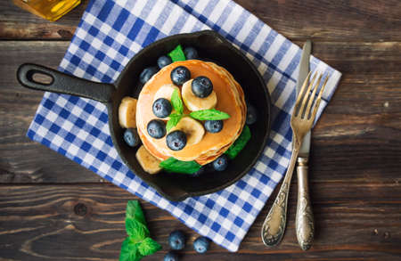 Stack of homemade pancakes in iron skillet with blueberries, banana and mint leaves on rustic woodenの写真素材