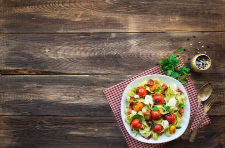 Fettuccine pasta with baked tomatoes, bacon and mozzarella cheese on rustic woodenの写真素材