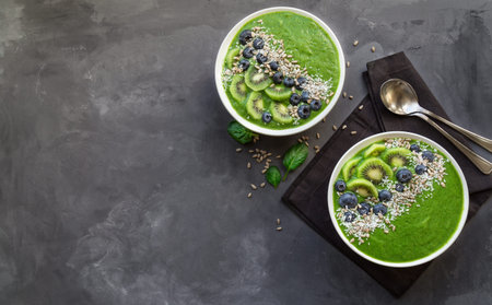 Breakfast green smoothie bowls with kiwi, blueberries and sunflower seeds on gray concrete