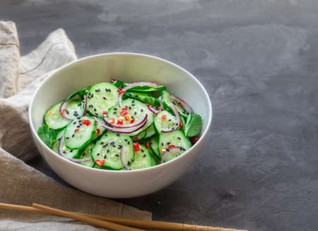 Asian cucumber salad with red onion, chilli pepper and black sesame in white bowl on gray concreteの写真素材
