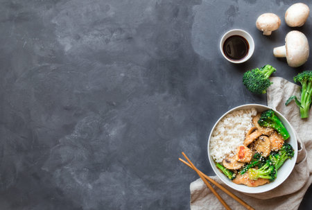 Teriyaki chicken, broccoli and mushrooms stir fry with white rice in bowl on gray concrete