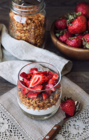 Homemade granola, muesli with chocolate chips, strawberries and yogurt in glass on rustic wooden