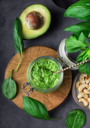 Fresh homemade vegan pesto sauce with basil, spinach, cashew nuts and avocado in jar on gray...