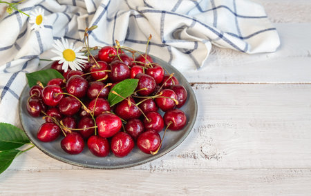 Fresh organic sweet cherries on plate at white wooden background.
