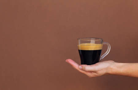 Cup with espresso coffee in woman's hand on brown background. Space for your text.の写真素材