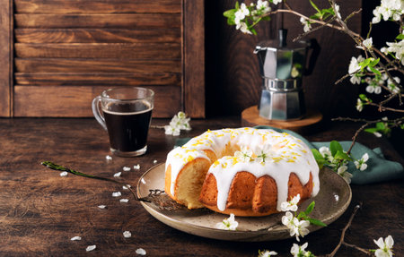 Fresh homemade lemon bundt cake decorated with white glaze and zest on rustic wooden background with...
