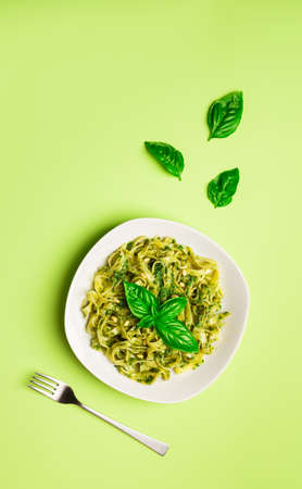 Tagliatelle pasta with pesto sauce, basil and pine nuts on light green background. Italian cuisine. Top view. Flat lay minimalist design.の写真素材