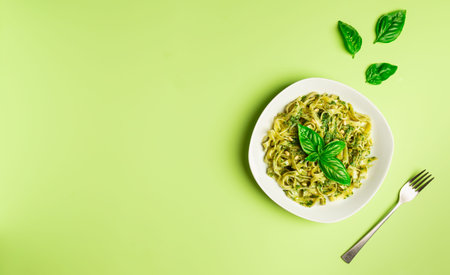 Tagliatelle pasta with pesto sauce, basil and pine nuts on light green background. Italian cuisine. Flat lay minimalist design. Top view. Space for text.の写真素材