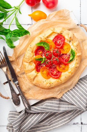 Fresh homemade galette with tomatoes, ricotta cheese and basil on white tile background. Top view.の写真素材