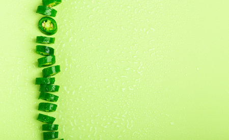 Pieces of green chili peppers lying on color background with water drops. Minimalist flat lay with...
