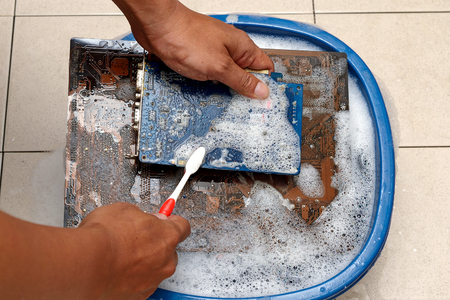 man cleaning computer mainboard with water and toothbrushの写真素材