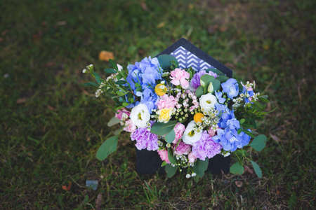 Image of beautiful flowers arrangement with blue hydrangea, white eustoma, spray yellow and violet roses, pink carnations, eucaliptus, waxflowers. Beautiful mixed flowers bouquet in black envelope box on a green grass backgroundの写真素材