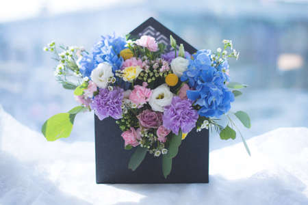 Image of arrangement with hydrangea, eustoma, spray yellow and violet roses, pink carnations, eucaliptus, waxflowers. Lovely Mixed flowers bouquet in black envelope box on window backgroundの写真素材