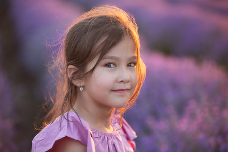 Beautiful Little girl in the lavender field. Close-up portrait of cute kid girl in the purple dressの写真素材