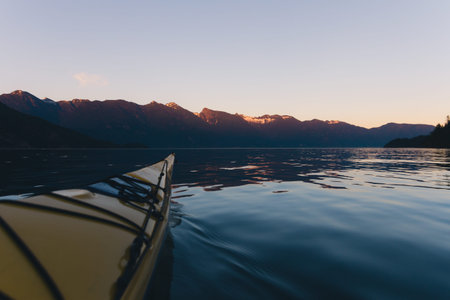 Kayaking alone on calm water with mountains in the background while sunset