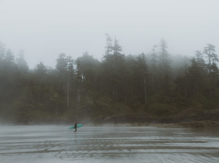 Surfer walking on beach in fogの写真素材