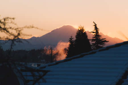 Snow covered forest and mountains illuminated by sunriseの写真素材