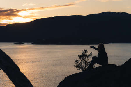 Woman on cliffs while sun behind mountainsの写真素材