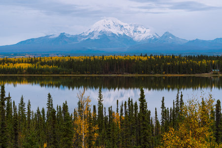 Alaskan mountains with glaciers, trees and snow caps in autumn season during sunset reflecting in lakeの写真素材