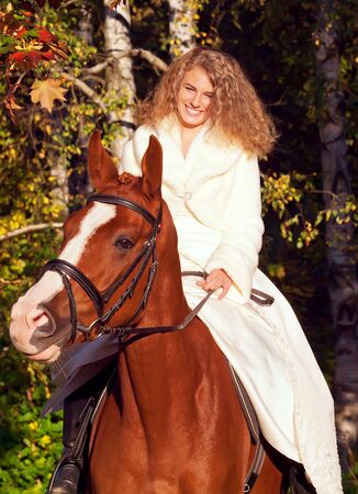smiling young bride ride on red  horse in forestの写真素材