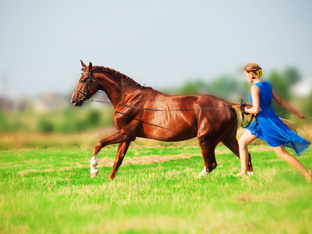 Running young beautiful  girl  with her horse in fieldの写真素材