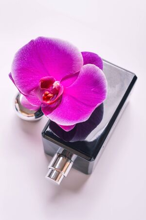 Black fragrance bottle with purple orchid around white. Flat layの写真素材