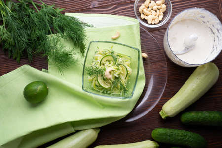 Detox vegetarian raw eating salad with zucchini and cucumber with cashew sauÑe. served in beautiful bowl on white table with green napkin. flat layの写真素材