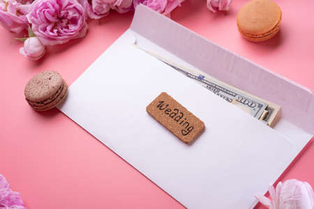 white envelope with cash around roses and macaroons against pink background. life style conceptの写真素材