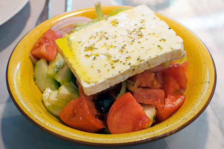 Traditional Greek salad with feta in a yellow plate. Delicious salad with cheese, vegetables and...