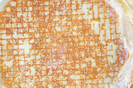 A thin pancake background. Cooking thin pancakes with holes in the pan. Fried buttered pancake view...