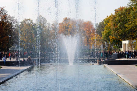 Fountain in a city park, close up. A fountain against a background of trees covered with autumn foliage and people walking in the park. Rest zone.の写真素材