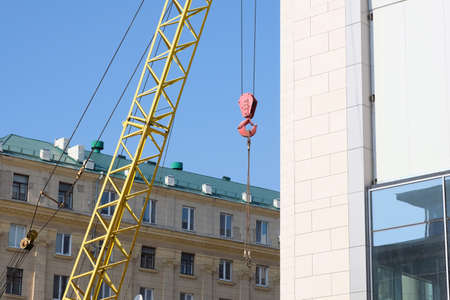 Close-up crane hook. A crane with a red hook on the background of multi-storey residential buildings. Building robots in the city.の写真素材